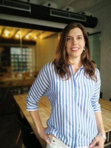 A woman in blue and white stripes shirt smiles posing to the photo in front of an empty desk