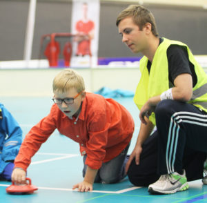 Kid prepares to throw a disk, assisted by an adult wearing a green bib